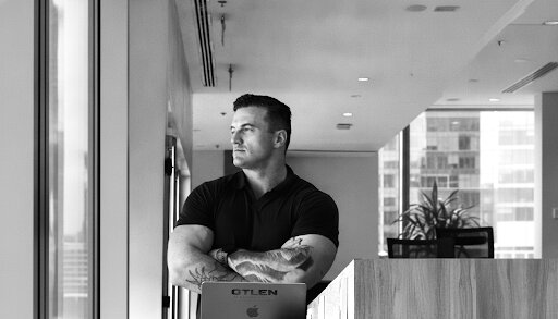 James Richman standing with arms crossed in an office, beside a laptop marked OTLEN.
